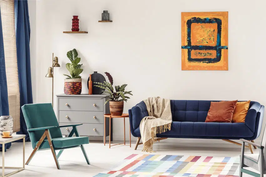 Rom with blue couch, sofa chair, rug, dresser, end table, and plants