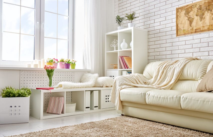 Living room with couch, floor rug, open shelf, white tile wall, and triple pane windows