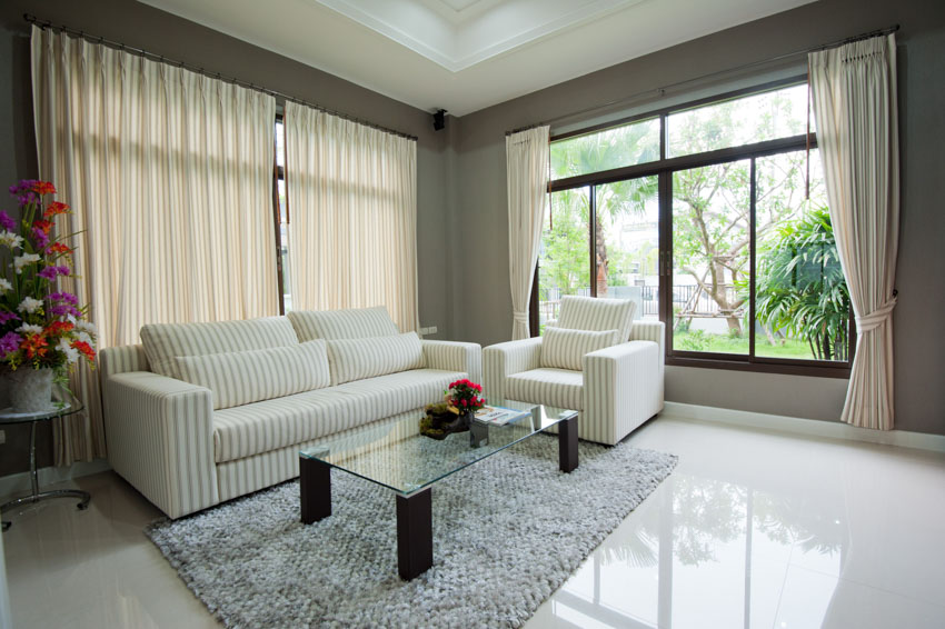 Living room with glass coffee table, white couch, floor, rug, porcelain flooring, windows, and curtains