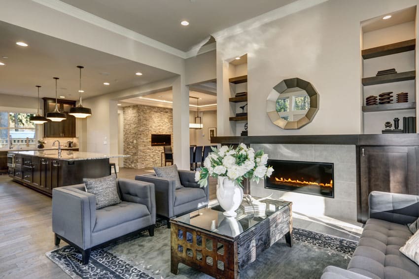 Living room with gray sofa chairs, glass coffee table, fireplace, dining area, center island, and hanging lights