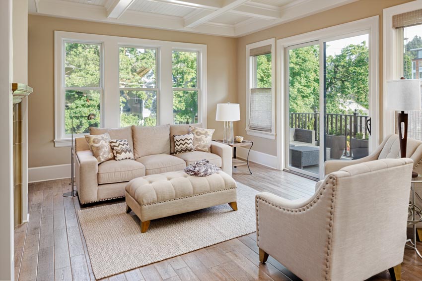 Room with wood floor, rug, sofa, ottoman, lamp, sofa chairs, and white framed windows 