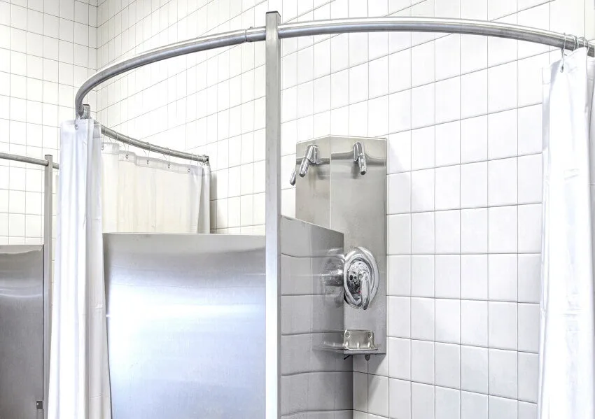 Locker room shower with tile walls and floor, and round shower curtain rods