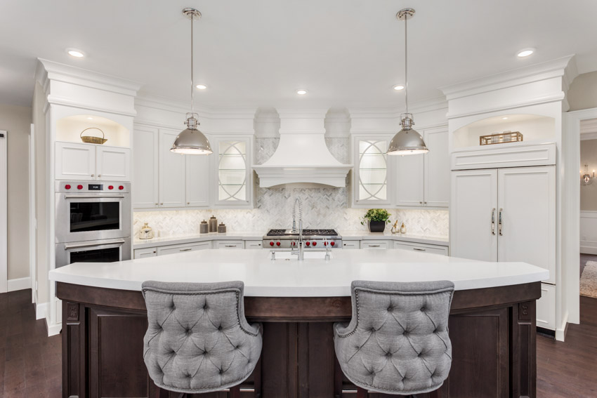Luxurious kitchen with Carrara marble backsplash, center island, pendant lights, chairs, cabinets, and range hood