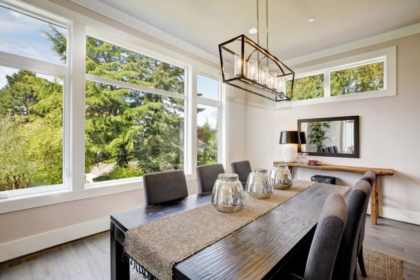 A black dining table illuminated by a rectangular chandelier 