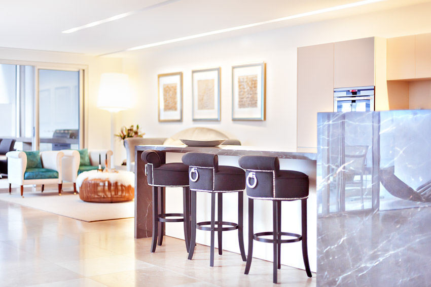 Luxury home bar with living area, windows, and cushioned upholstered bar stools