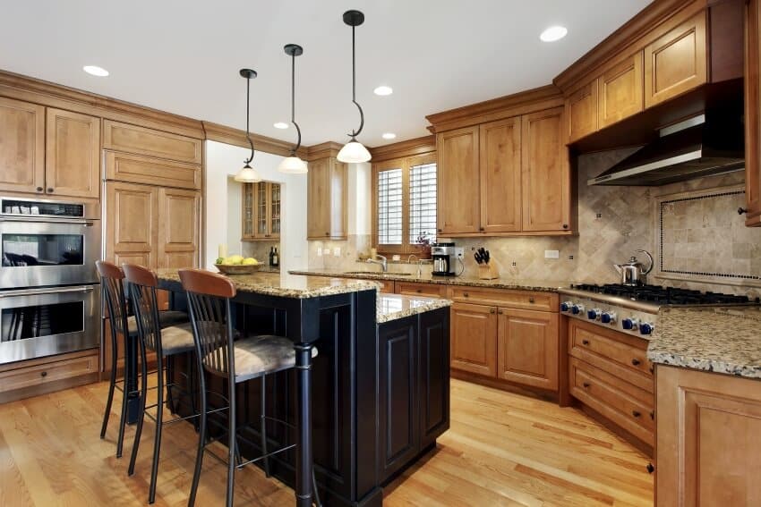 A luxury kitchen with granite island, tall black chairs and alder wood cabinetry