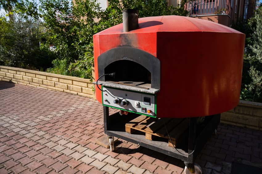 Metal pizza oven with controls placed in backyard area with brick pavers