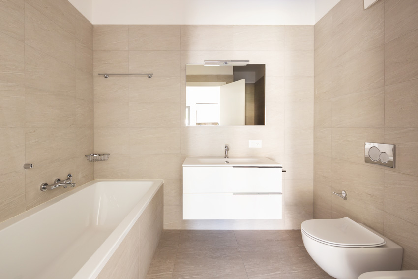 Minimalist bathroom with toilet, tub, floating vanity, and limestone walls