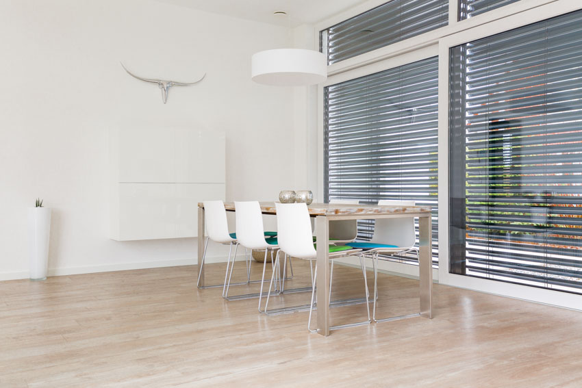 Minimalist dining room with wood floors, window blinds, table, chairs, and pendant light