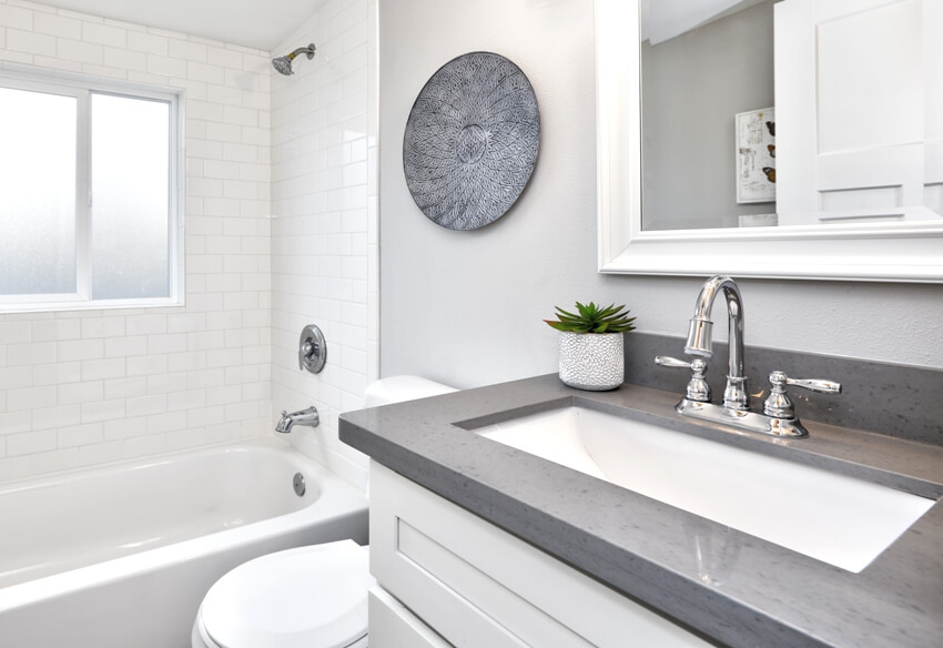 Modern bathroom interior with white vanity topped with gray laminate countertop, bathtub and a toilet