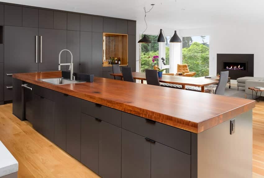 Modern kitchen featuring island with ipe countertop, black cabinets, and wooden floors