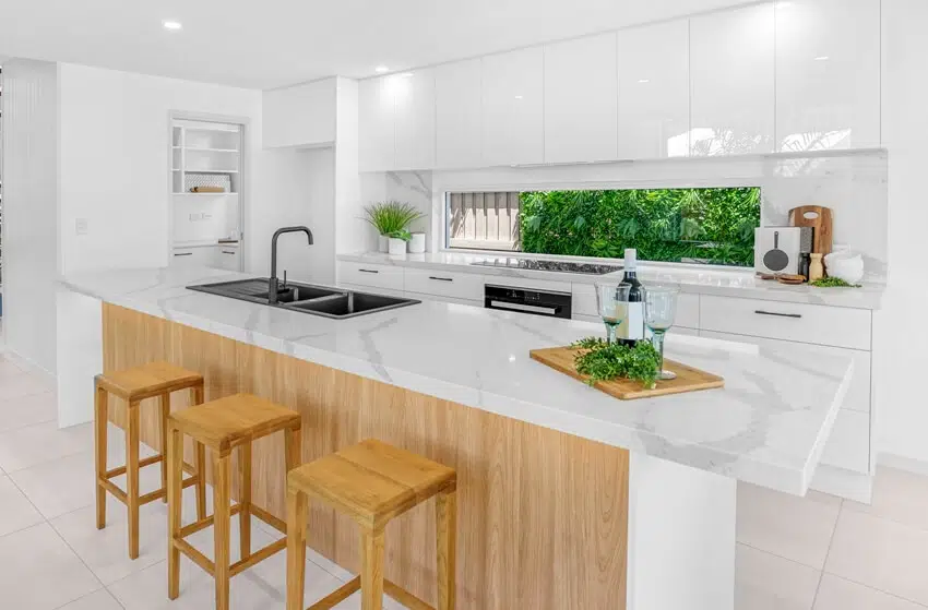 Kitchen with white marble counters, wood stools and handleless cabinets