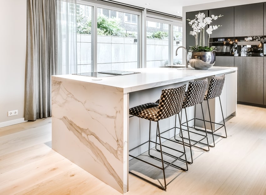 A modern kitchen with polished calacatta marble countertops, chairs and grey cabinets