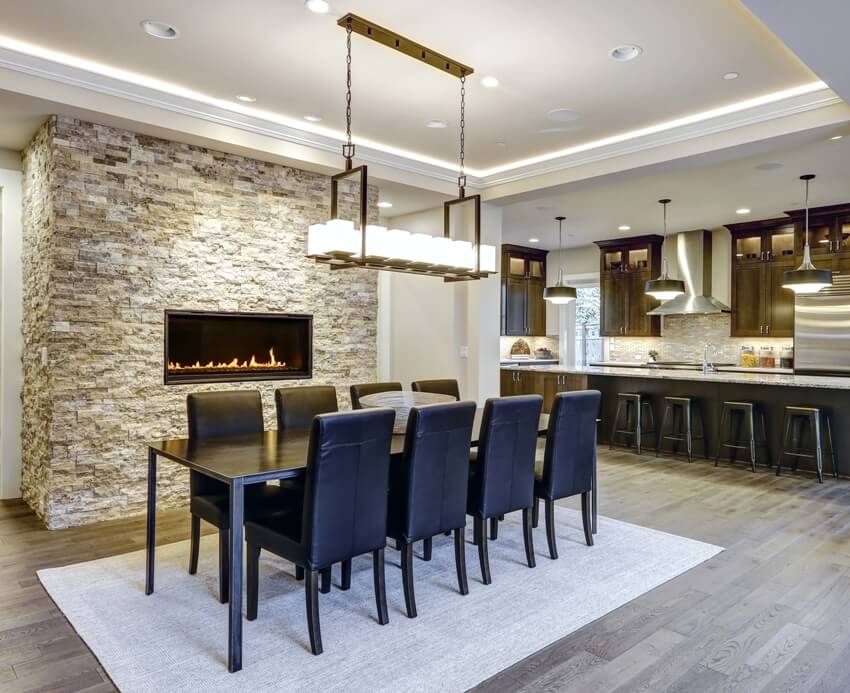 A modern open floor plan dining room design accented with stone fireplace wall facing black dining table lined with leather chairs and illuminated by rectangular chandelier