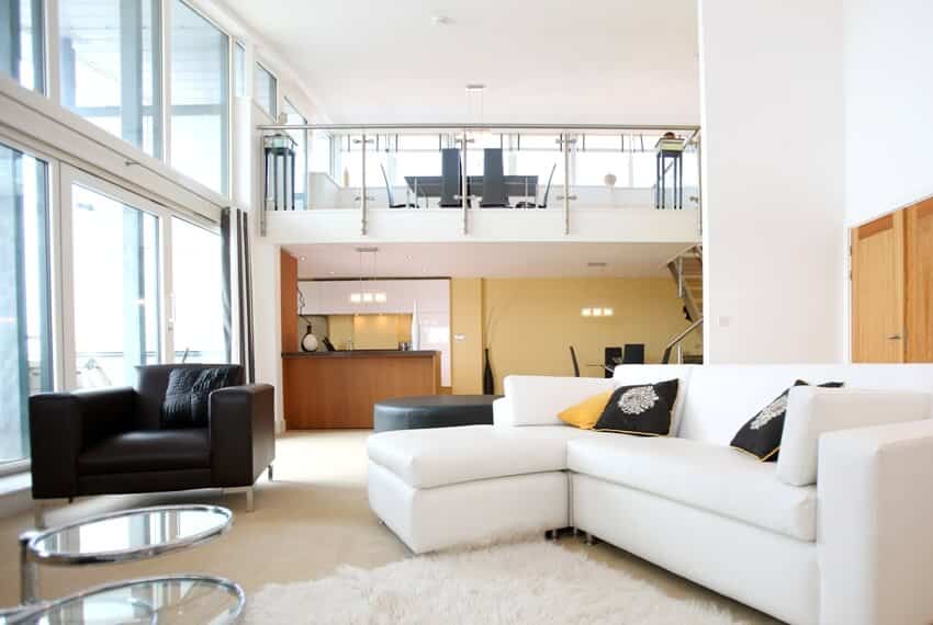 A modern open plan apartment with living room in foreground and mezzanine balcony with dining set