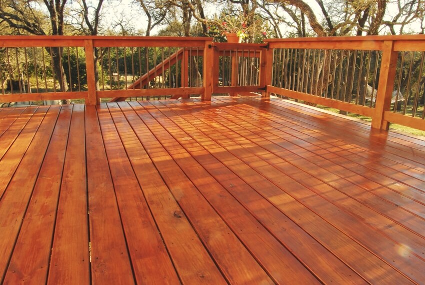 Newly stained outdoor wooden deck surrounded with trees on a sunny afternoon
