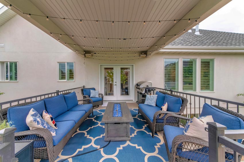 Outdoor deck with carpeted floor, fire pit table, blue cushioned couch, and canopy roof