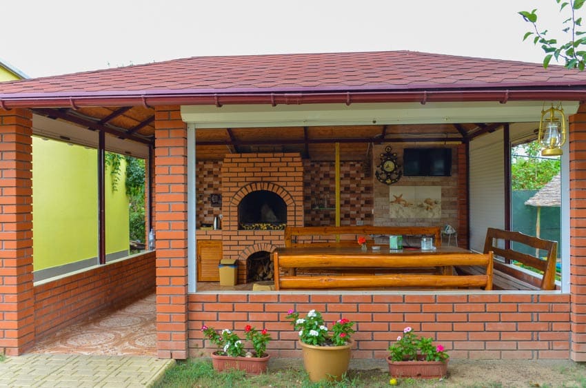 Outdoor dining area with brick fireplace, pizza oven, wood benches, and table