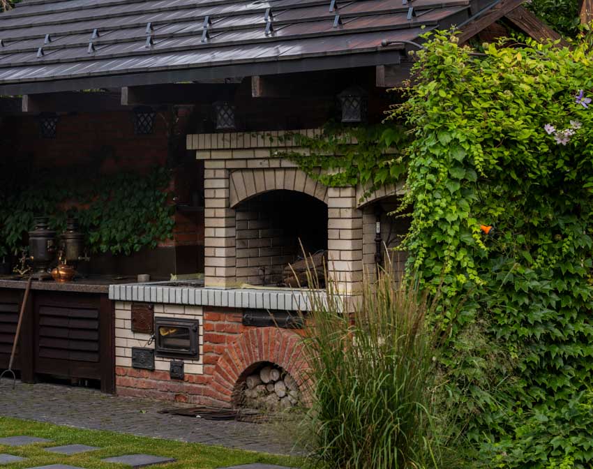 Outdoor kitchen with basic fireplace design, pizza oven, and plants