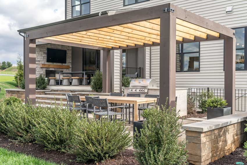 Outdoor patio with pergola, table, chairs, hedge plants, and white siding wall