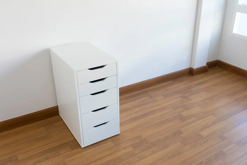 Room interior with wood floor, white wall, and filing cabinet