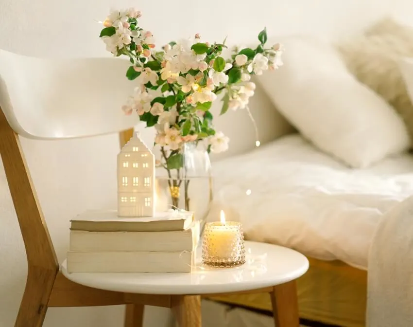 Scandinavian bedroom interior with book, votive candle holder and vase with apple spring flowers on a chair