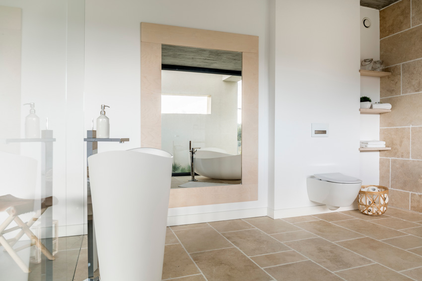 Spacious bathroom with limestone tiles, floors, mirror, shelves, and toilet
