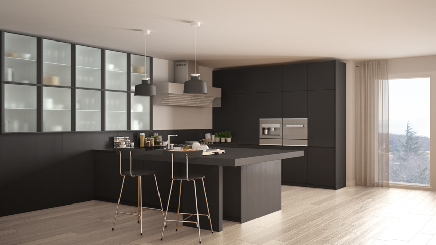 Spacious kitchen with black island, brass bar stools, hanging lights, wood flooring, and windows