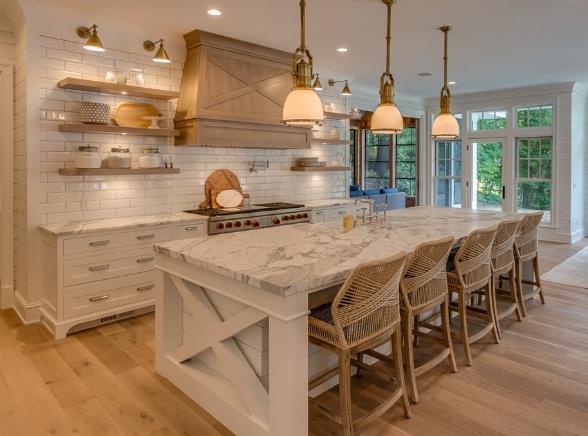 Stunning kitchen with three pendant lights hang over the island with honed calacatta marble countertop and decorative vent hood over the stove