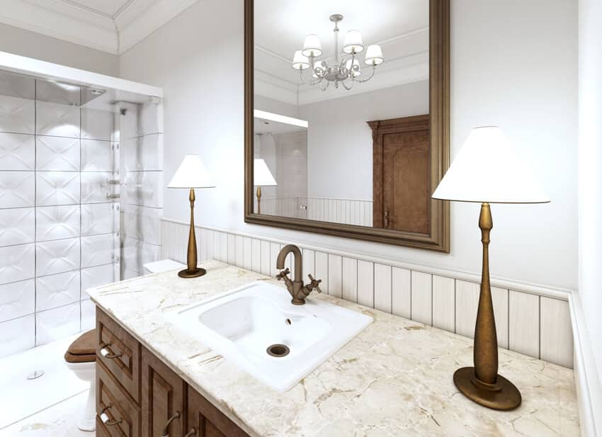 Bathroom with calacatta oro marble countertop with sink, two table lamps and a large mirror in a brown frame