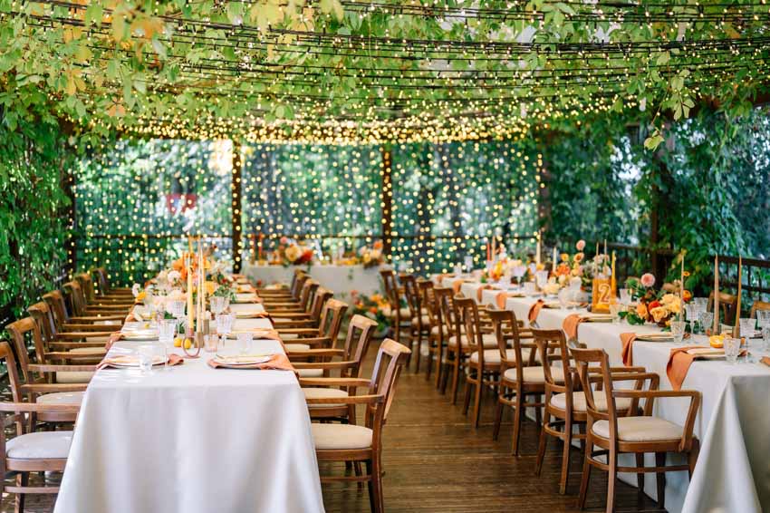 Wedding reception area with banquet tables, wood flooring, chairs, string lights, and decor pieces