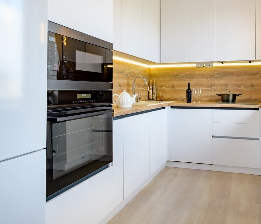 A well designed white and wooden beige modern kitchen interior with built in microwave and oven