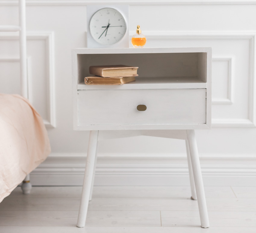 White Scandinavian bedroom nightstand with a clock and books