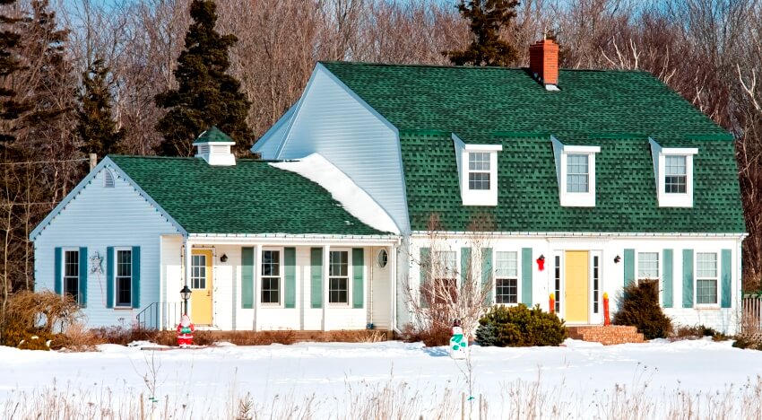 A gorgeous white house with many windows and green painted roof surrounded by snow