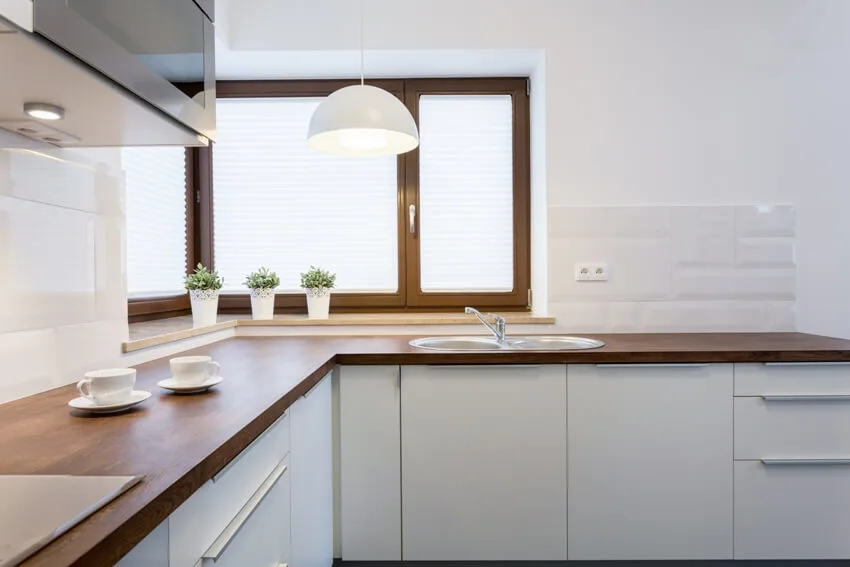 White kitchen with two teacups on ipe wood countertop and green plants on windows