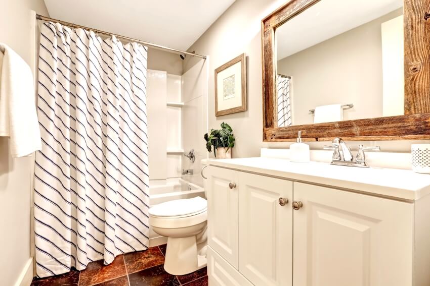 White tones bathroom with vanity cabinet, wooden framed mirror, and striped shower curtain