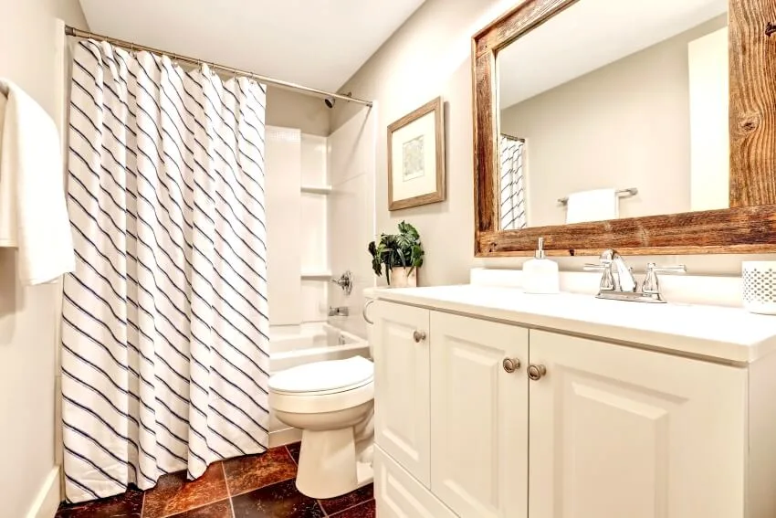 White tones bathroom with vanity cabinet, wooden framed mirror, and striped shower curtain