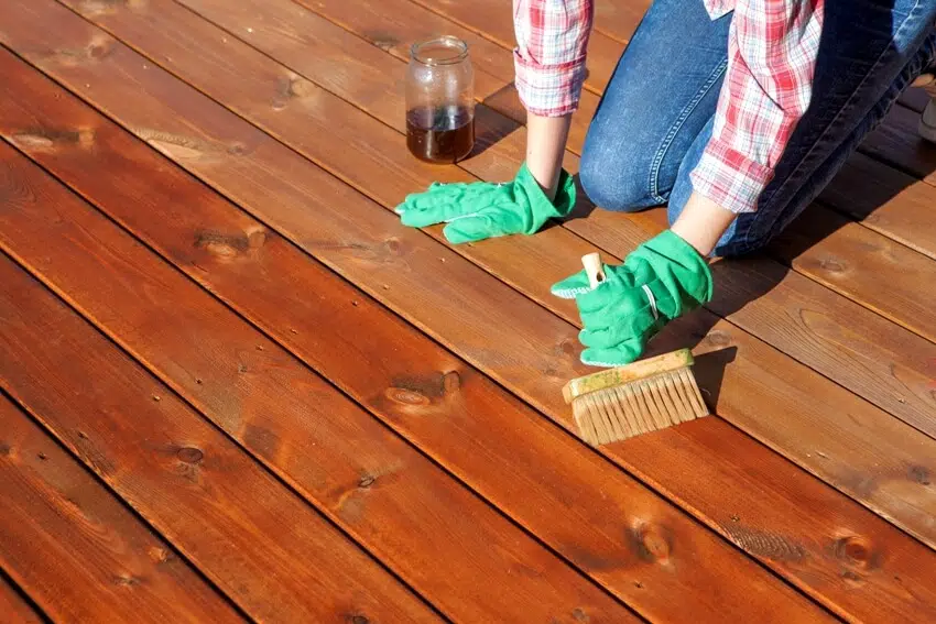 A woman applying protective varnish or wood oil on a patio wooden floor