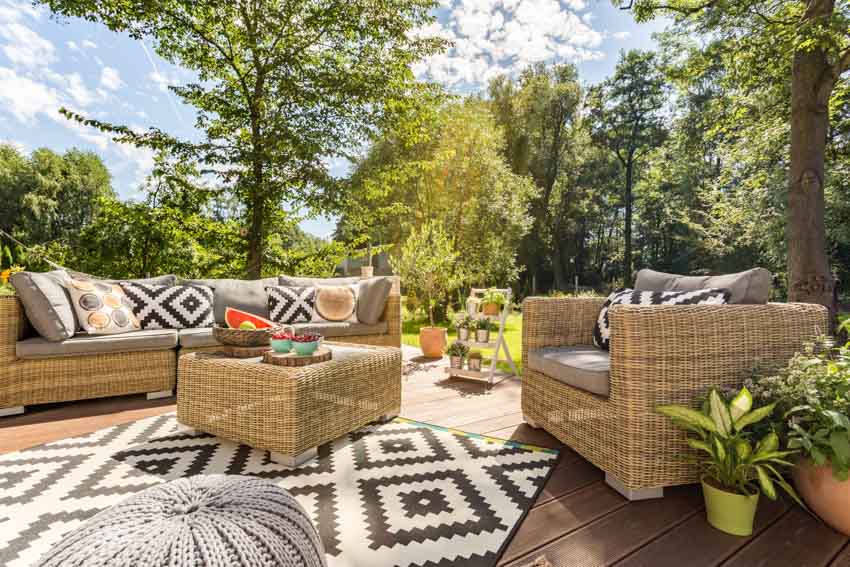 Wood patio with outdoor rug, wicker chair, couch, coffee table, and potted plants