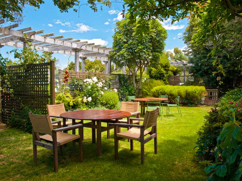 Backyard with table, chairs, pergola lattice privacy fencing, trees, flowers, and plants
