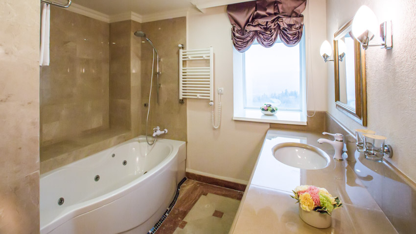 Bathroom with balloon Roman shades, tub, window, towel holder, countertop, sink, faucet, and mirror
