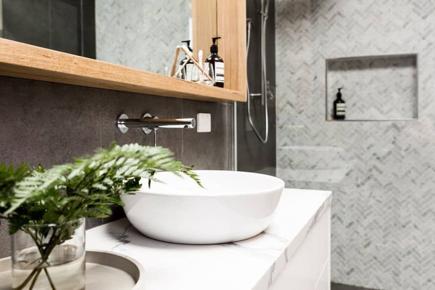 Bathroom with basin sink, wall-mounted faucet, quartz countertop, herringbone tile shower wall, and mirror