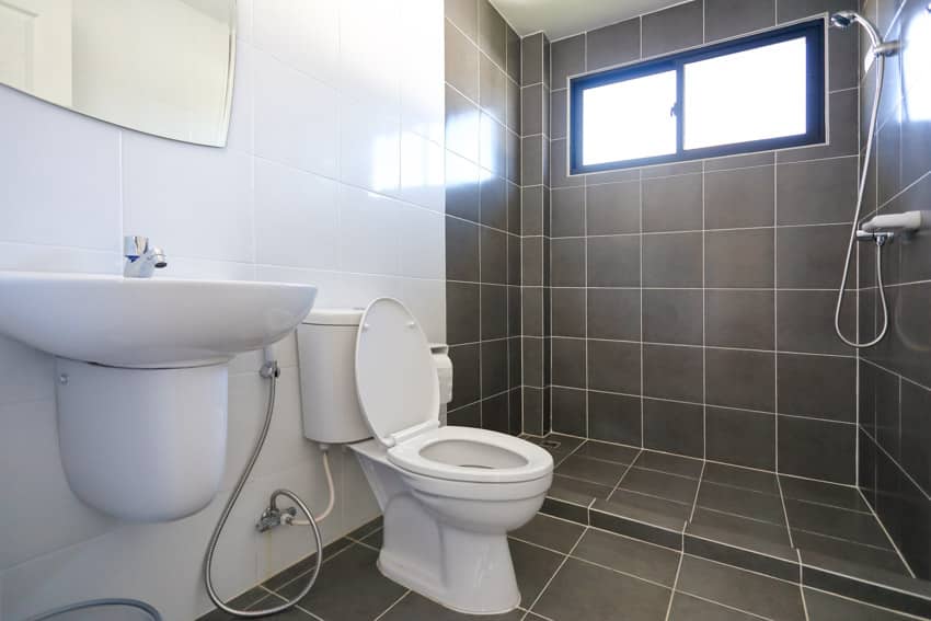 Bathroom with black floor to ceiling tiles, toilet, sink, bidet, shower, and mirror