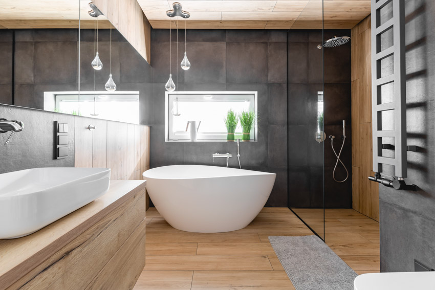 Bathroom with black large format tile, shower, tub, glass divider, vanity mirror, sink, wood cabinets, and windows