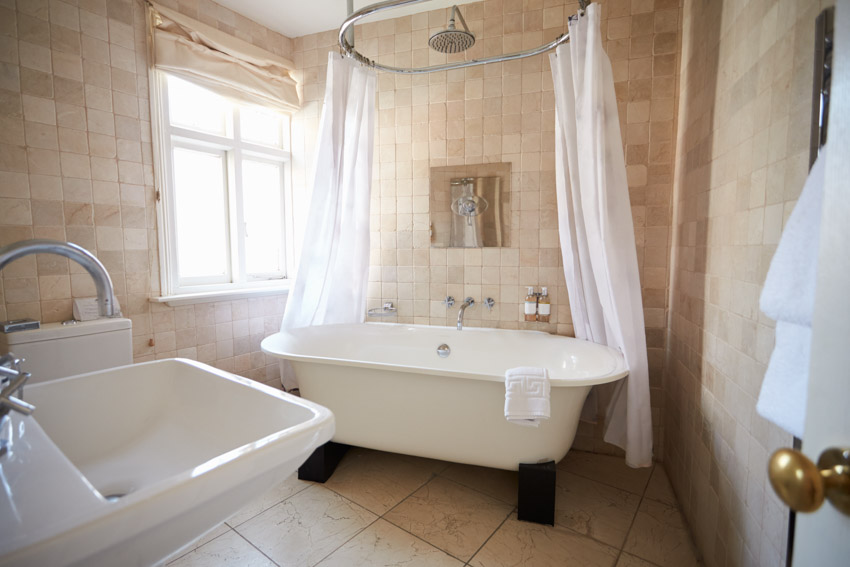 Bathroom with clawfoot curtain, tub, sink, tile flooring, and windows