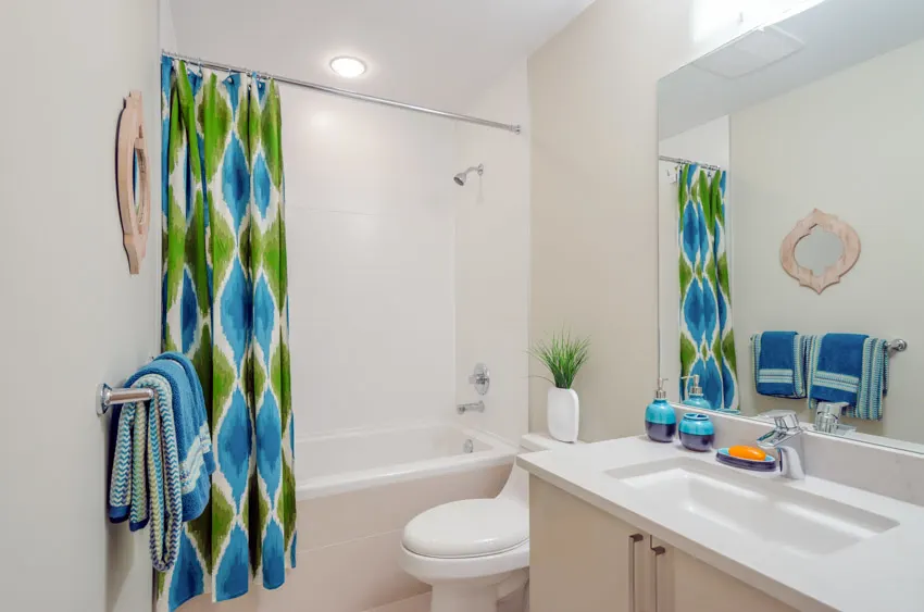 Bathroom with fabric curtain, white wall, mirror, countertop, sink and toilet