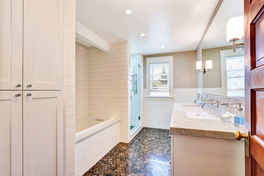 Bathroom with floor to ceiling tiles, tub, window, vanity area, ceiling lights, countertop, and mirror