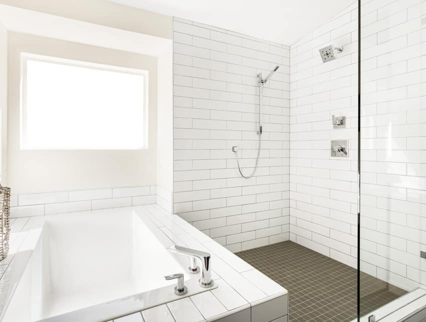 Bathroom with floor to ceiling tiles, window, dual shower, and tub