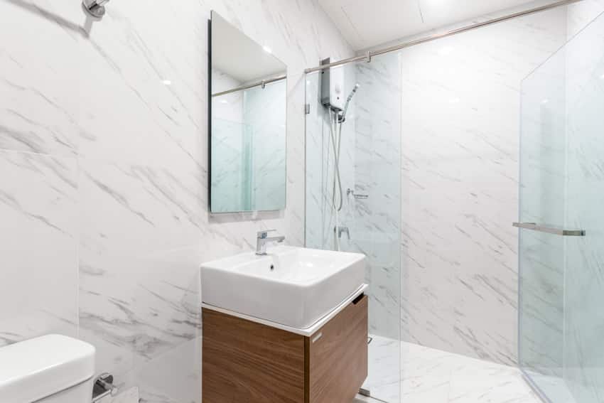 Bathroom with marble floor to ceiling tiles, sink, wood cabinet, mirror, glass door, and shower