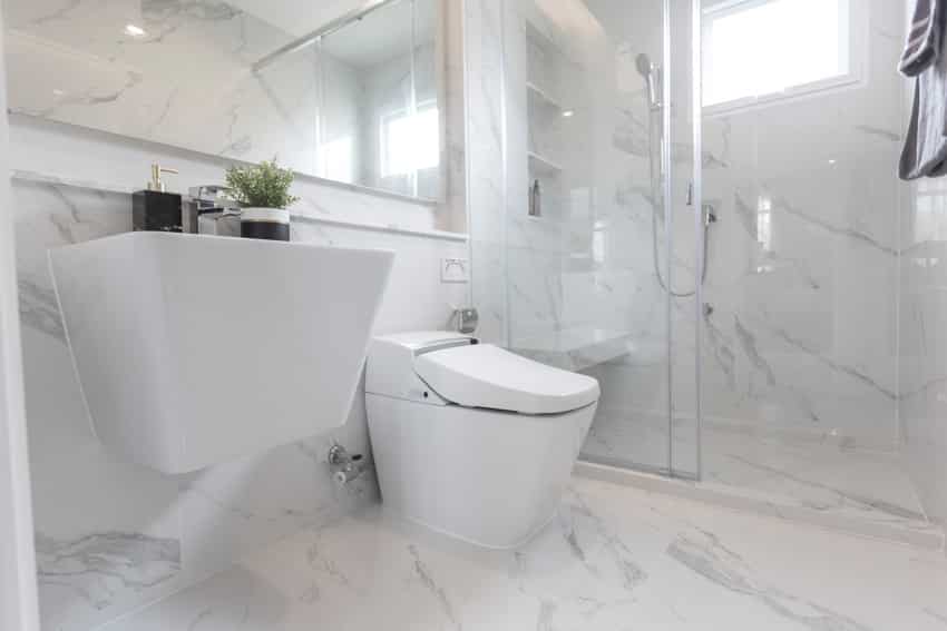 Bathroom with Platina Statuario marble wall, floors, toilet, sink, mirror, glass door, and windows